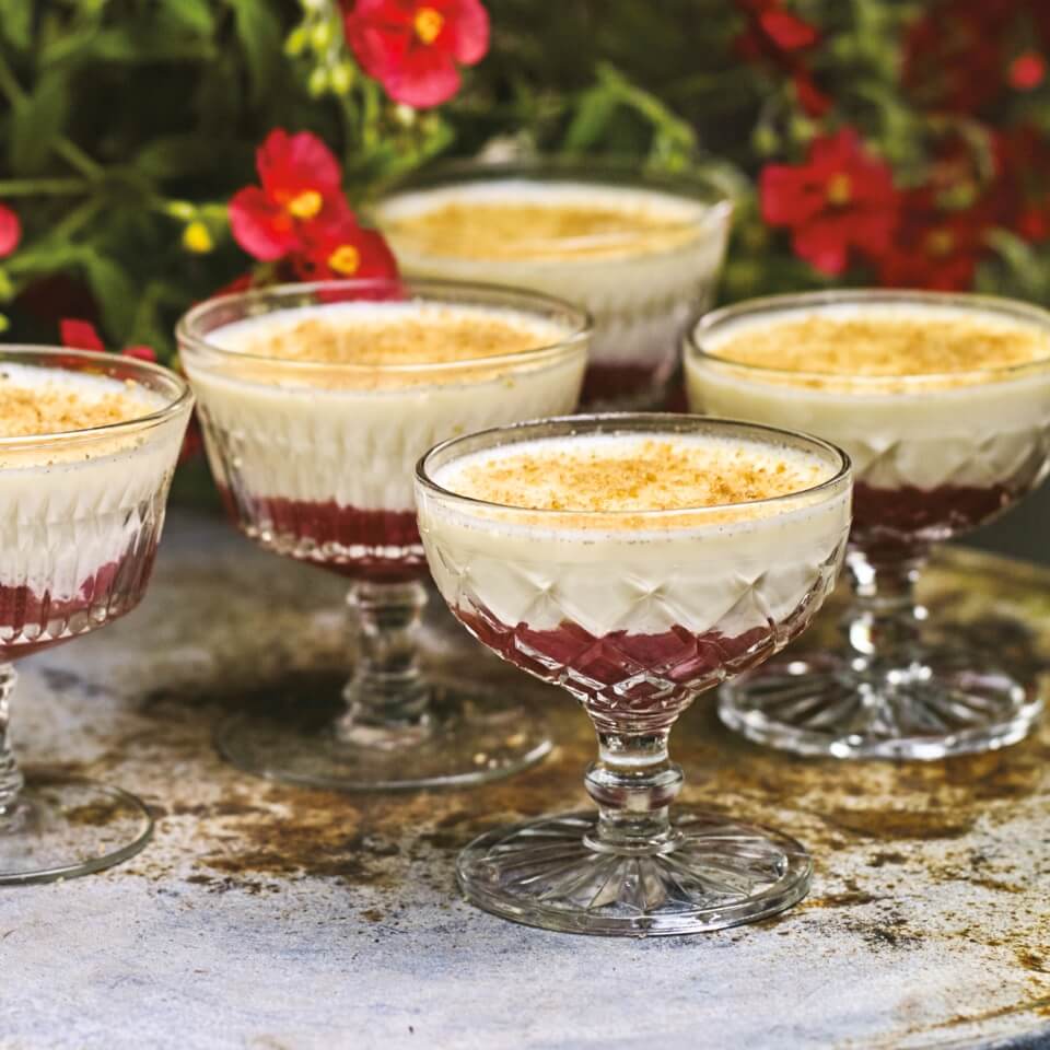 Glasses with a red panna cotta in an outside garden with red flowers behind them