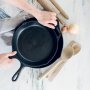 A person's hands holding a cast iron pan with wooden tools around it