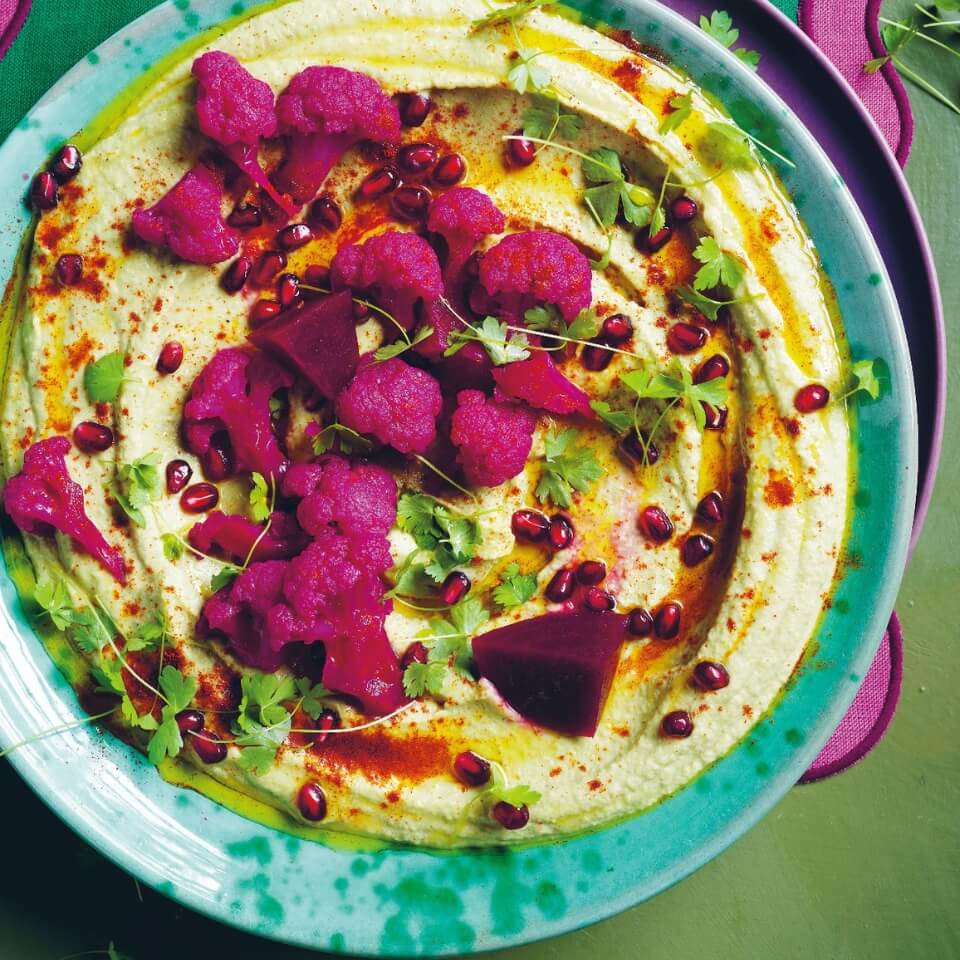 A blue dish of hummus on a patterned tablecloth