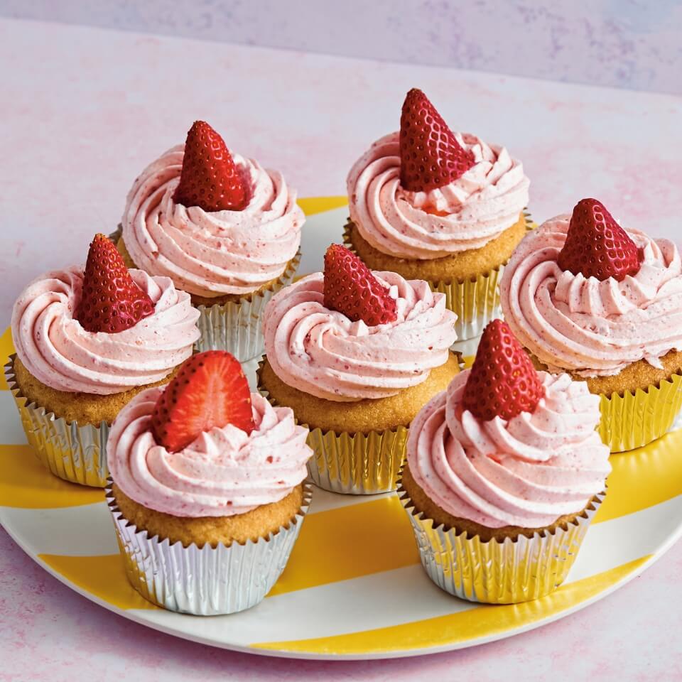 A plate of cupcakes with pink frosting and topped with strawberries