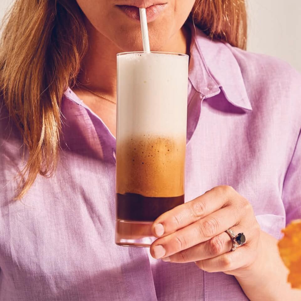 A woman in a light purple shirt drinking an iced cappuccino from a straw