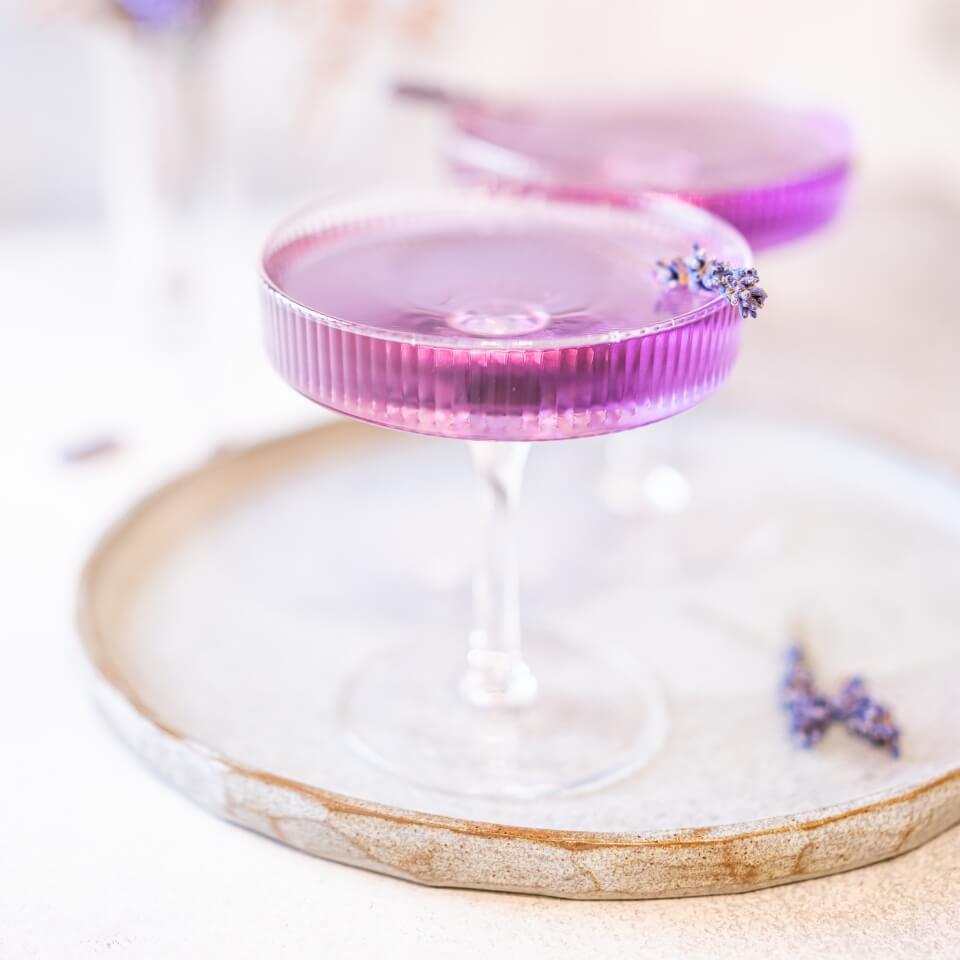Two purple martinis garnished with lavender on a serving tray