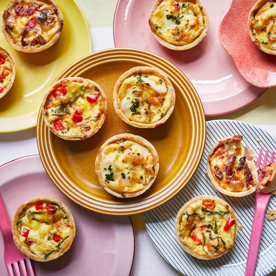 Assorted coloured plates with miniature quiches and a hot pink fork