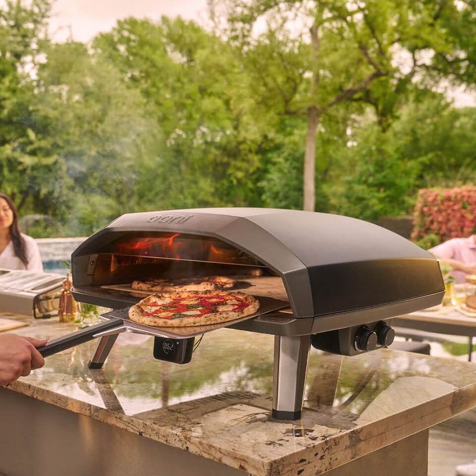 A person sliding a pizza out of an outdoor pizza oven