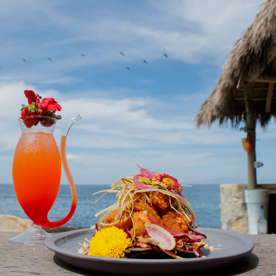 A plate of food and a strawberry cocktail on a surface overlooking the beach