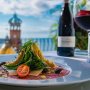 A view of a plate of food and a bottle and glass of wine on a patio overlooking the ocean