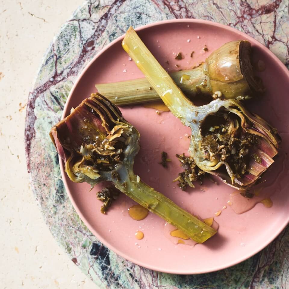 A pink dish with artichokes on a marble table