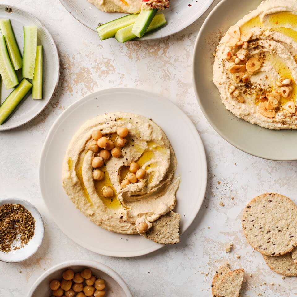 Dishes of hummus with different garnishes, vegetables and crackers