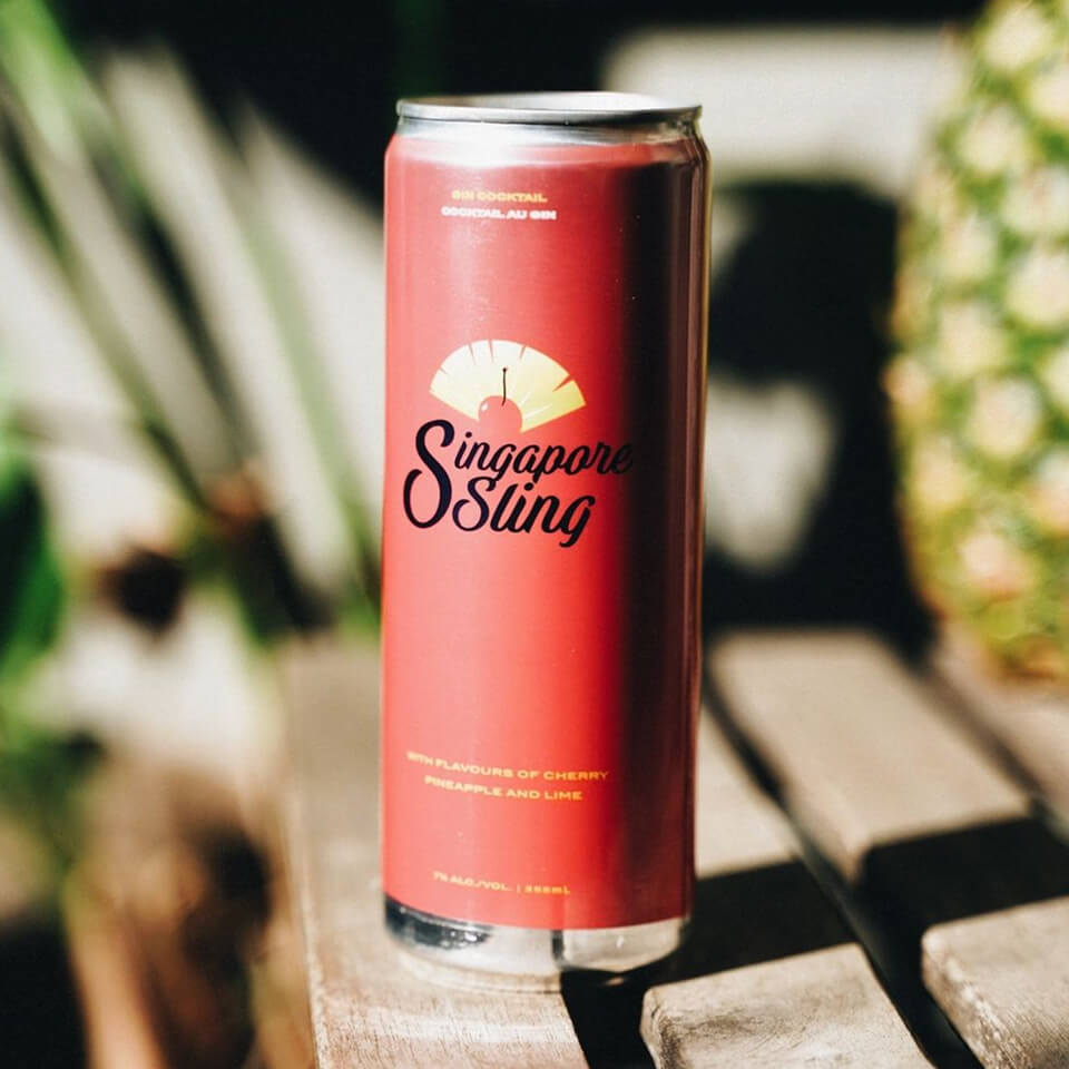 A red can on a wooden table with a pineapple and leaves visible in the background