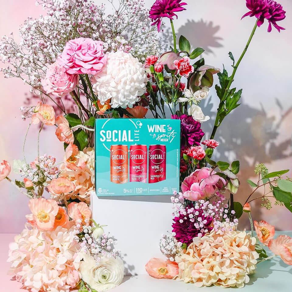 A blue box of canned wine spritzes with flowers around it