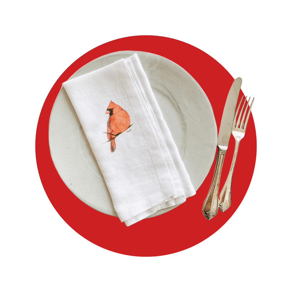 A plate with a napkin with a cardinal on it and cutlery over a red circle