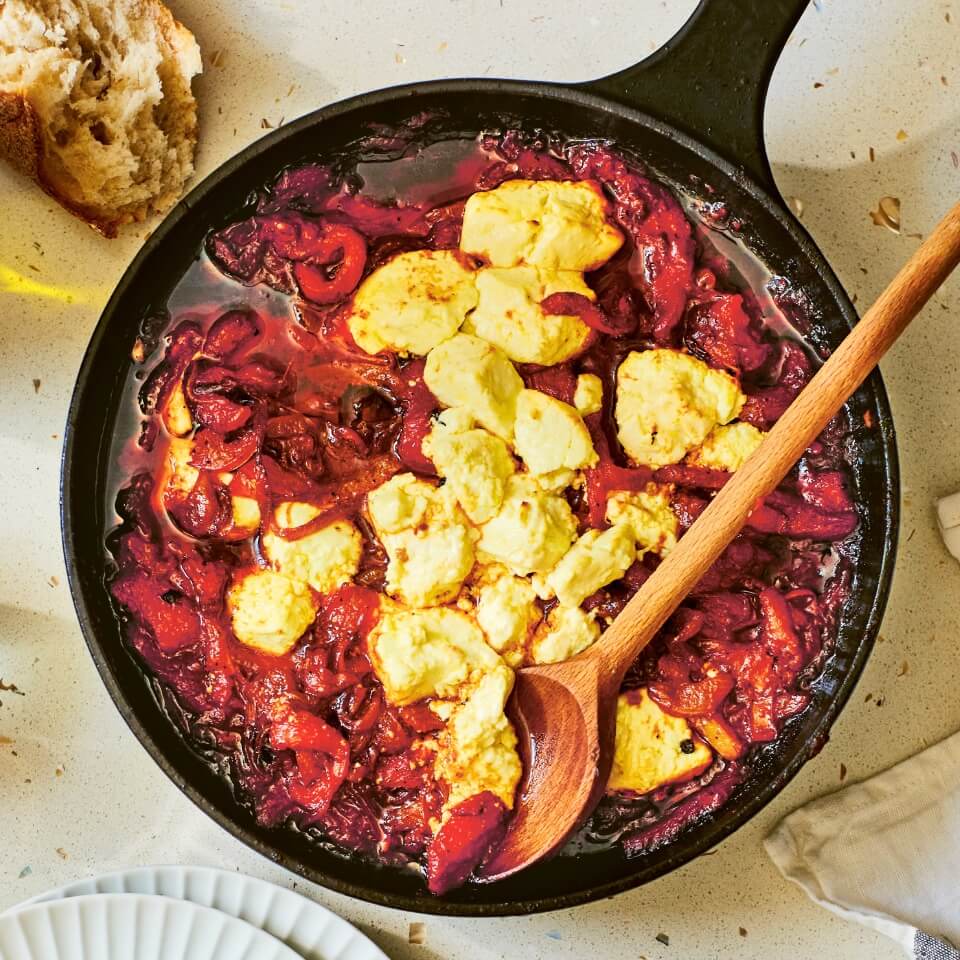 A pan with feta cheese, stewed peppers and a wooden spoon