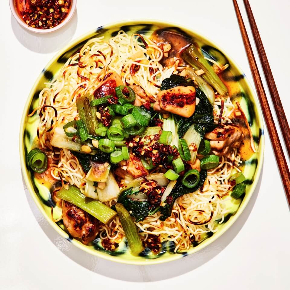 A dish with chicken chow mein, a side dish with sauce and wooden chopsticks photographed from above