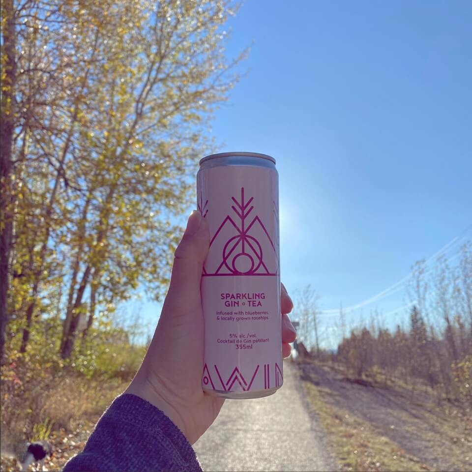 A person holding up a pink can on a trail with trees