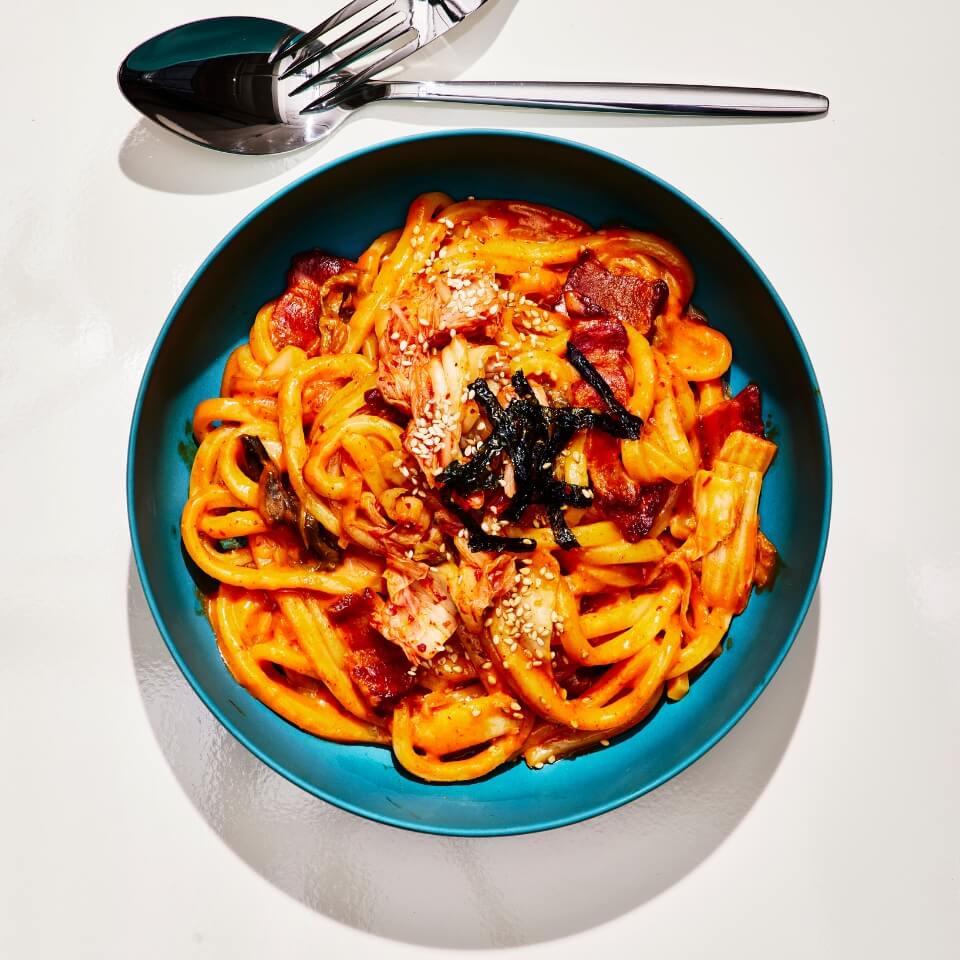 A blue bowl with noodles and a fork and spoon next to it