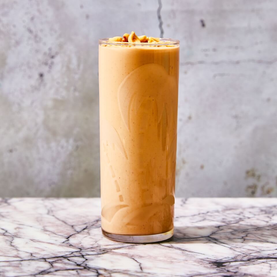 A glass of peanut punch on a marble surface with a concrete wall behind it