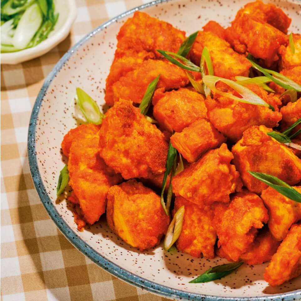 A bowl of tofu nuggets with bright orange sauce