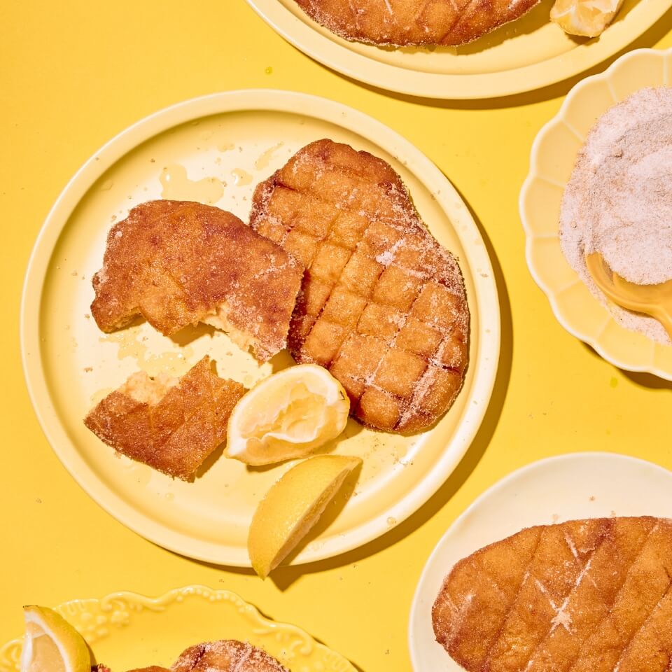 Beaver tail pastries with lemon slices on a yellow plate on a yellow surface