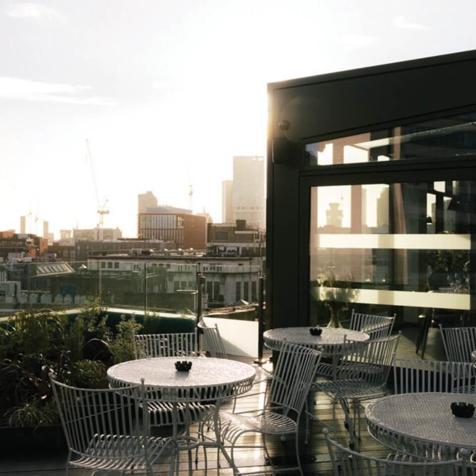 A patio on a rooftop with buildings and sunlight in the background