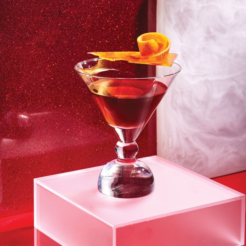 A cocktail garnished with an orange rim against a red-and-white background