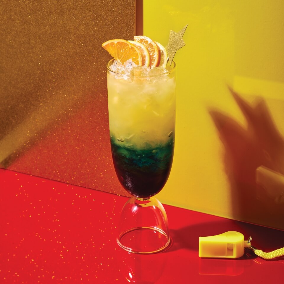 A green and yellow cocktail against a red and yellow backdrop