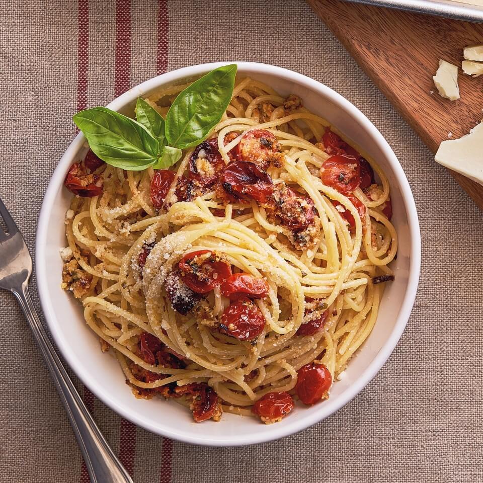 A white bowl with spaghetti and cherry tomatoes