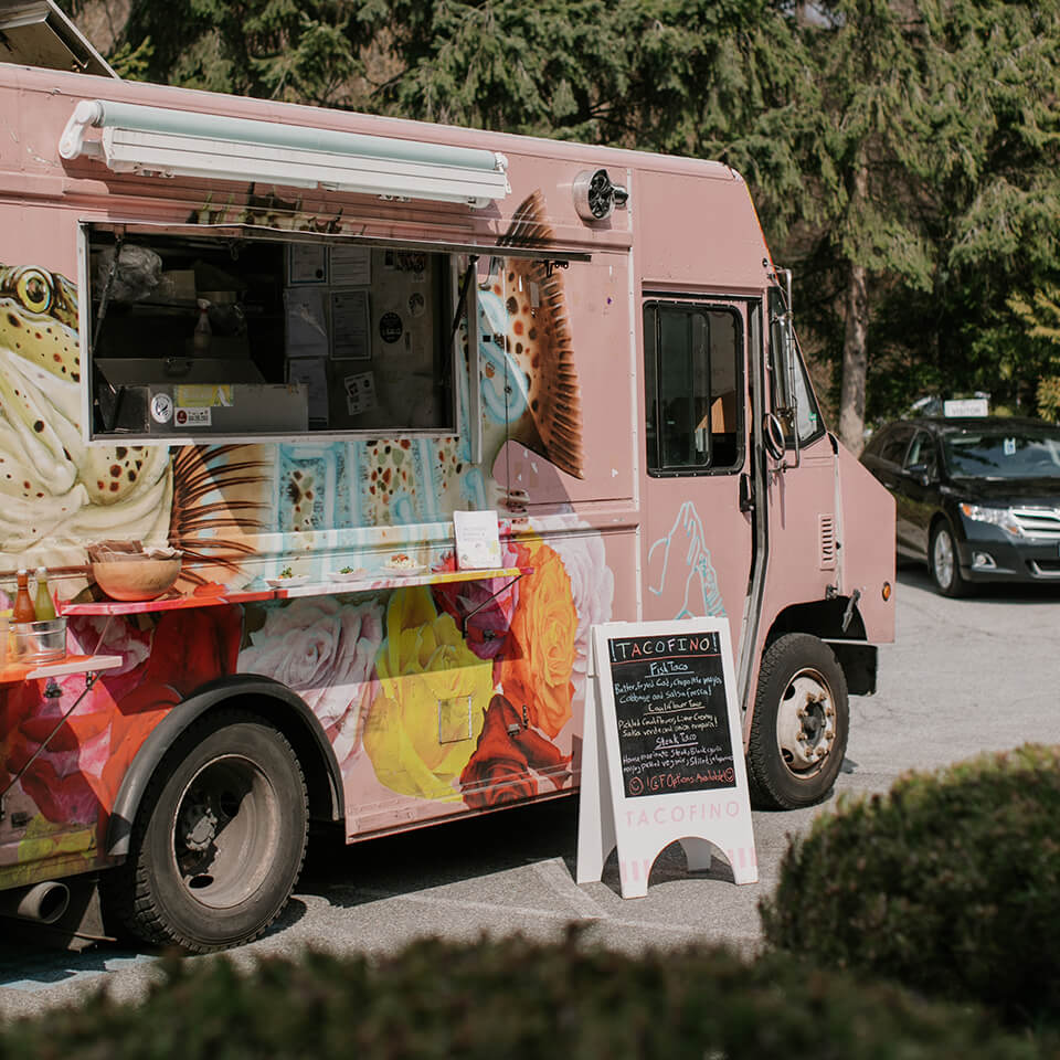 A pink food truck with a fish painted on it and a white folding sign