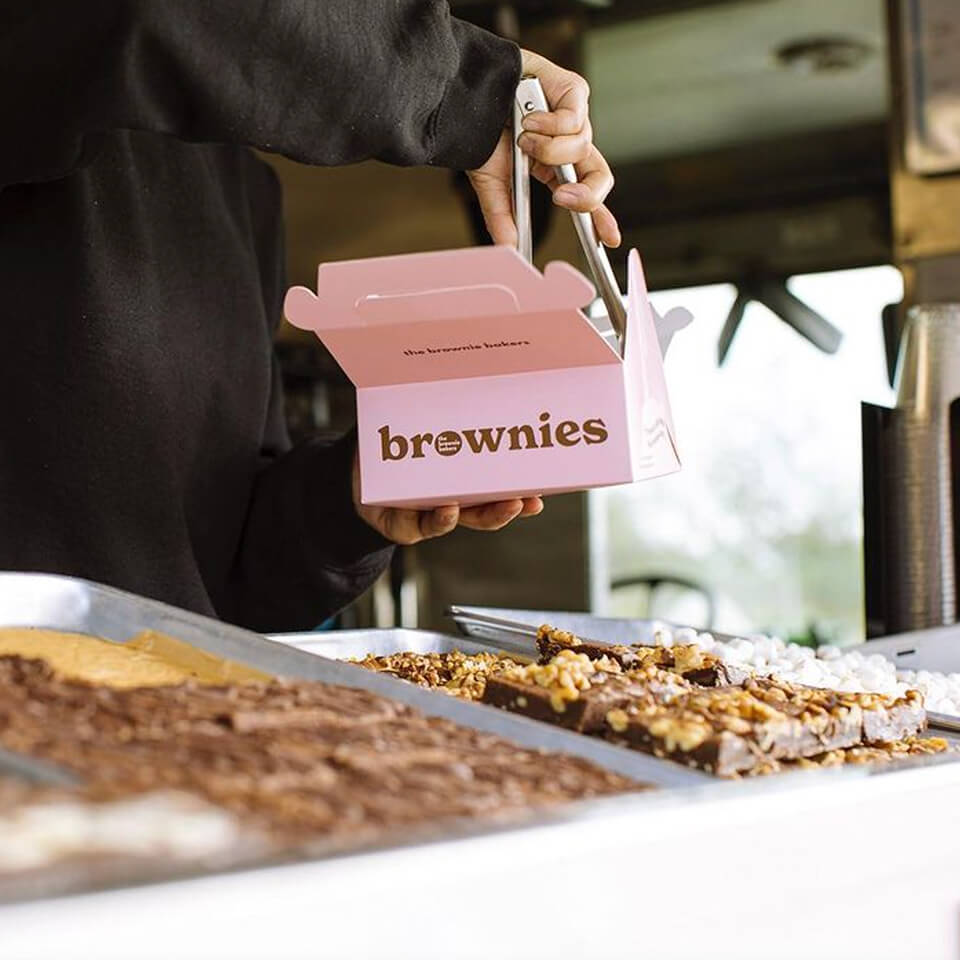A person using tongs to place brownies in a pink box