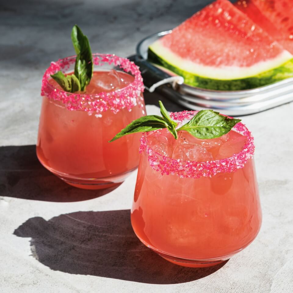 Two glasses with a cocktail and slices of watermelon behind it