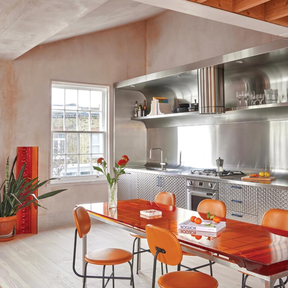 A view of a kitchen decorated in bright orange, light wood and stainless steel tones