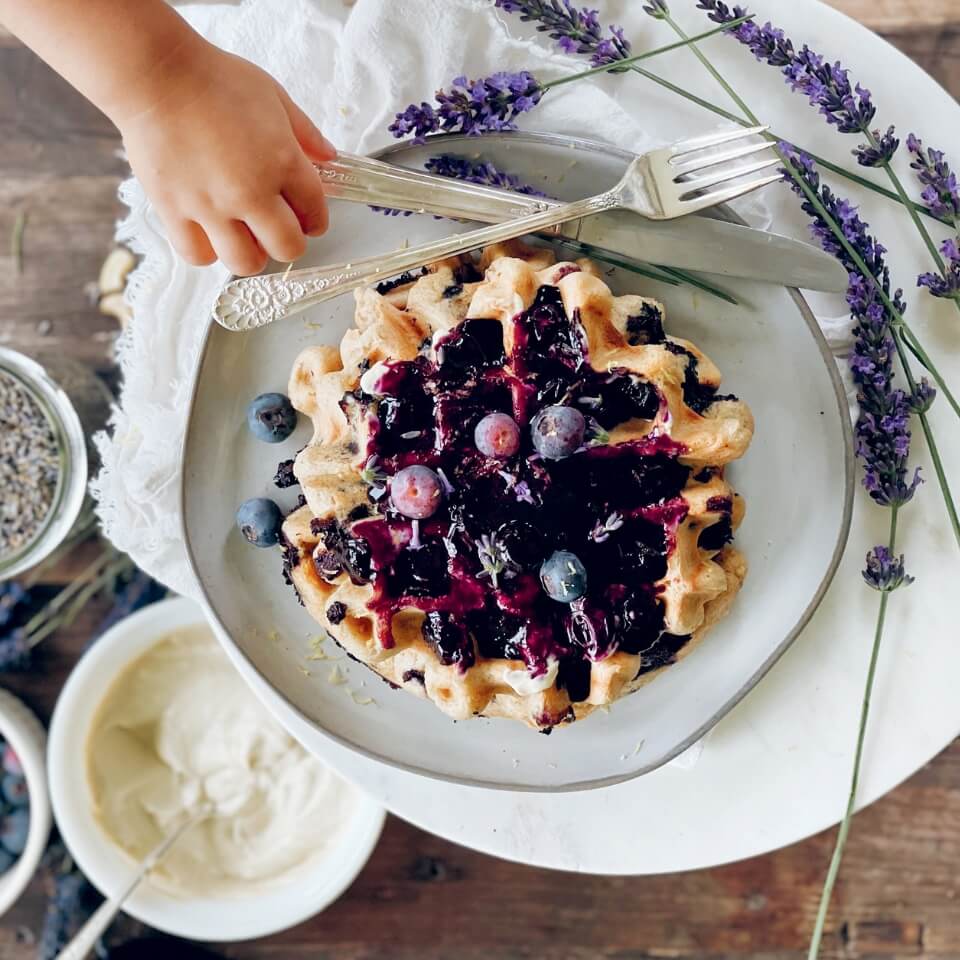 A child's arm and a plate of waffles topped with blueberry compote