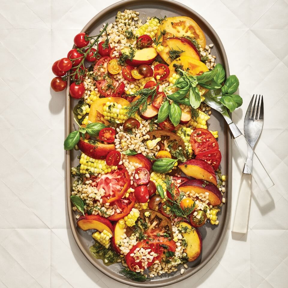 An oval-shaped dish with peach, corn and tomato salad, with forks next to it