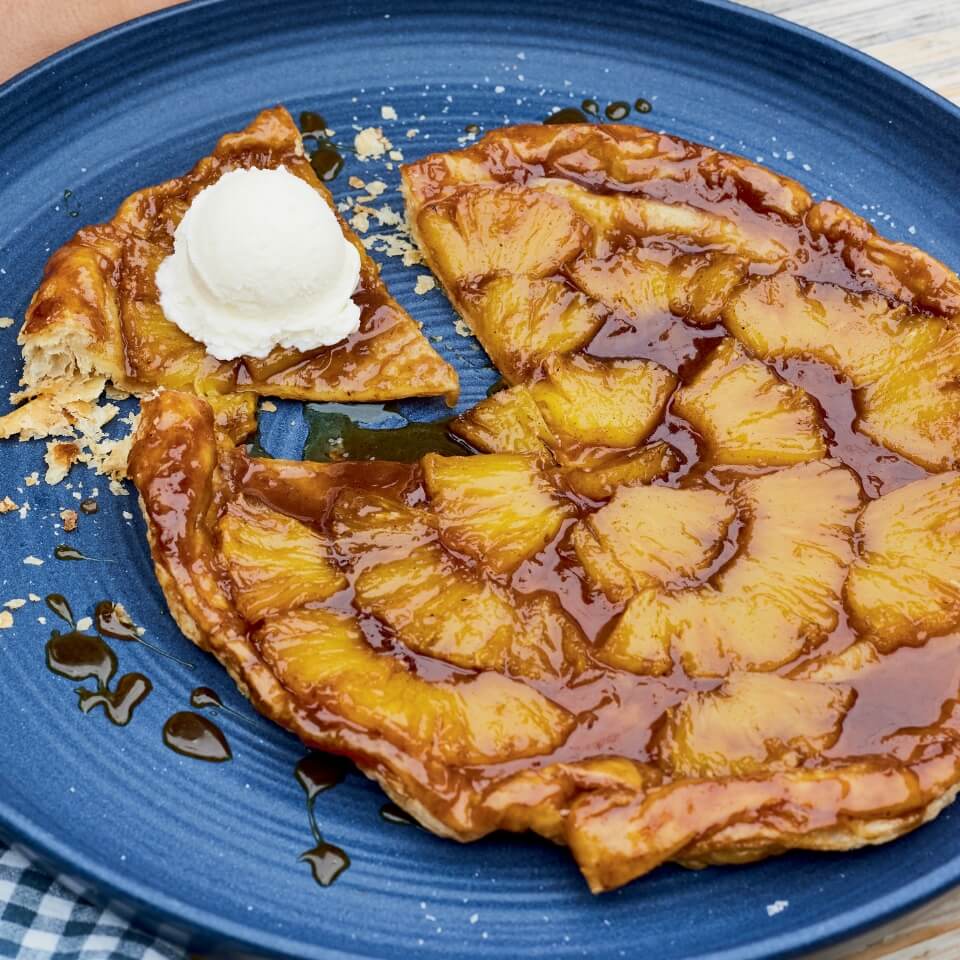 A pineapple tart with a scoop of vanilla ice cream on a blue plate