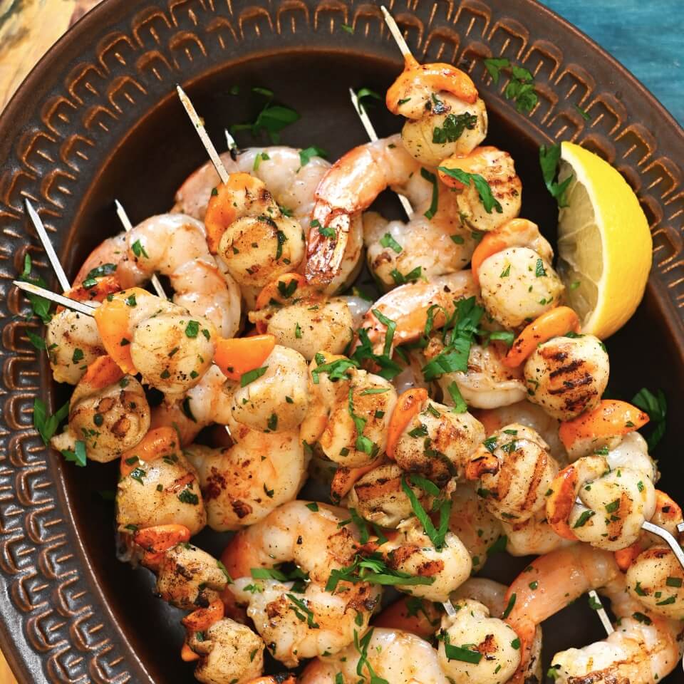 Shrimp and scallop skewers on a brown platter with a lemon wedge