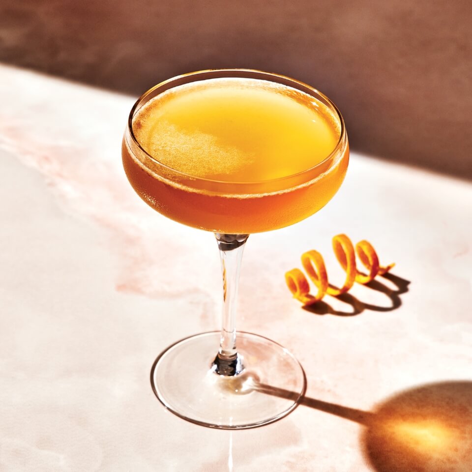 A Sidecar cocktail in a couple glass with an orange rind twist next to it