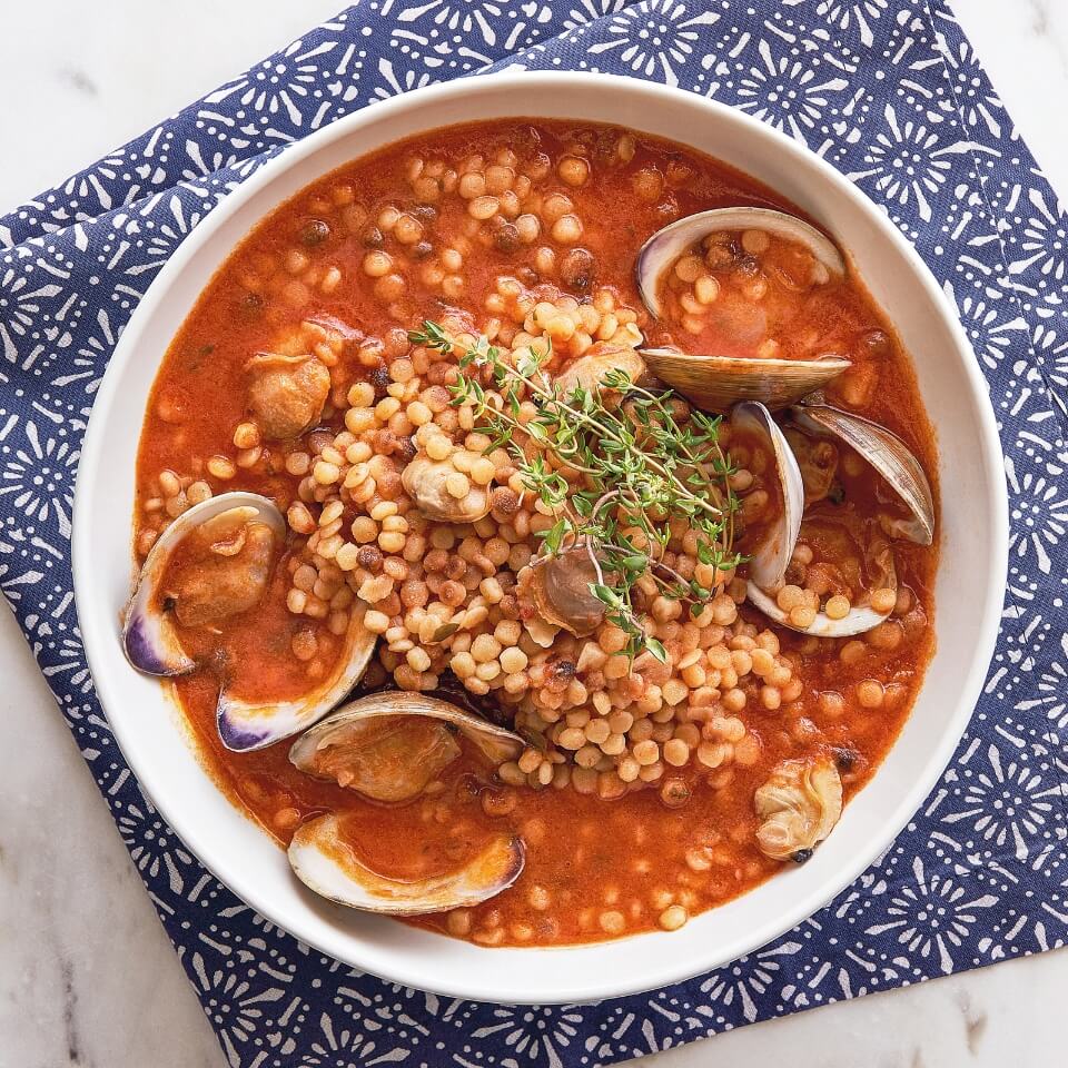 A bowl filled with tomato soup with fregola and clams