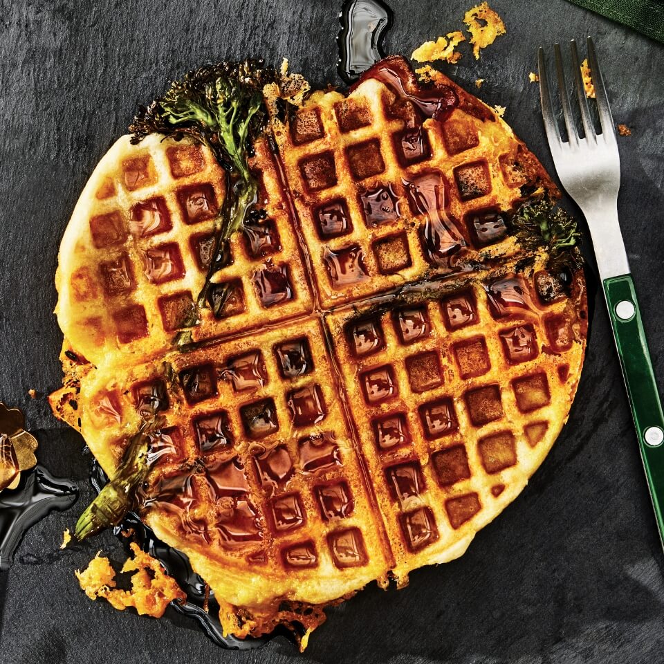 A waffle with broccolini and syrup with a fork next to it