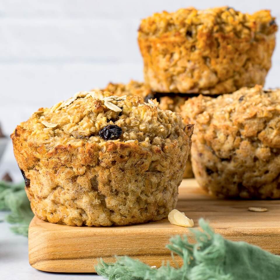 A muffin on a wooden cutting board with more muffins in the background