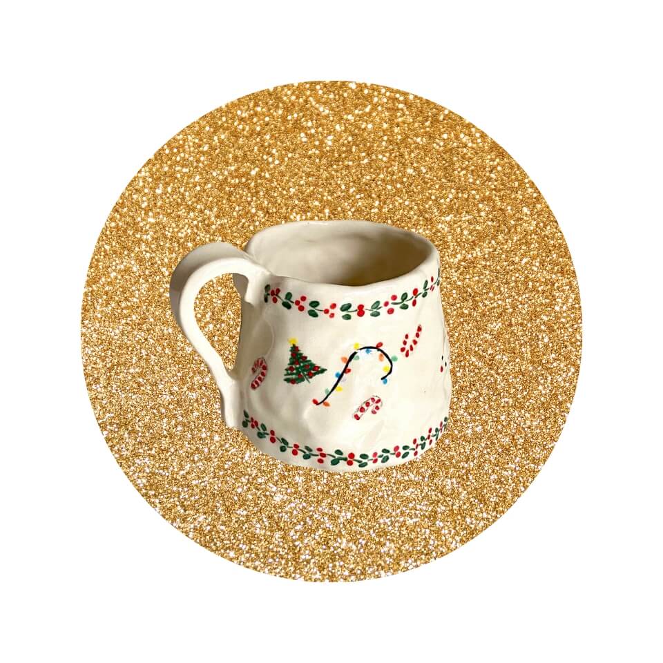 A white mug with a Christmas design in a sparkly gold circle