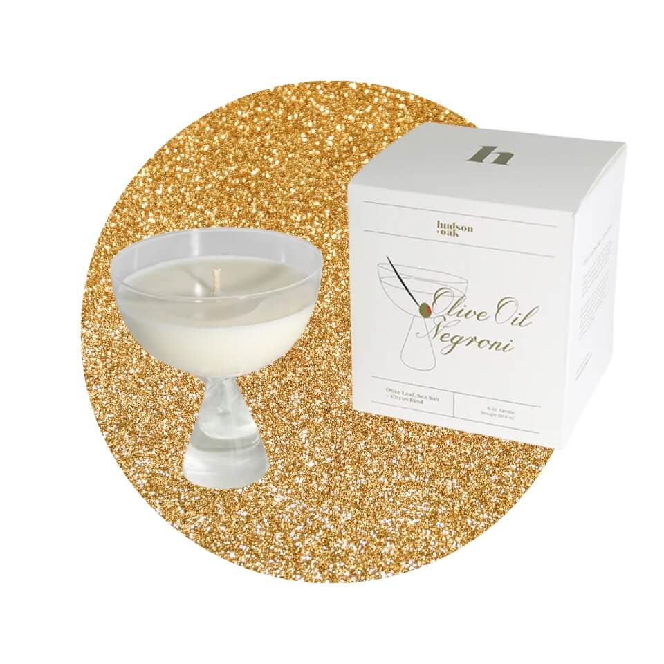 A candle in a coupe glass and a white box over a sparkly gold circle