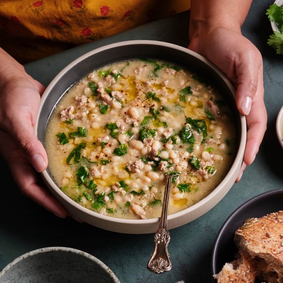 A person's hands holding a bowl of white chili