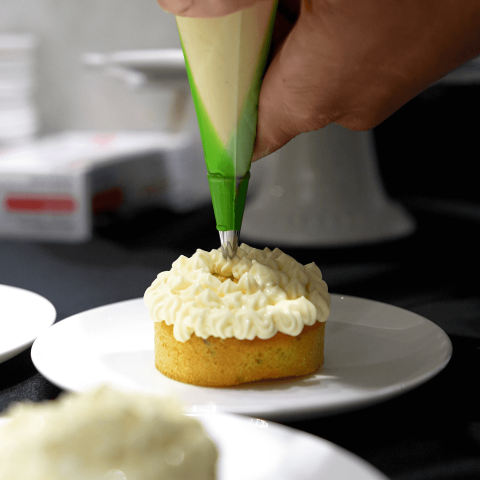 A person piping frosting onto a personal-sized sponge cake on a white plate