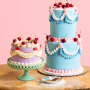 two pretty tiered cakes with cherries on a table