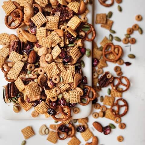 A recipe for Sweet and Salty Chex mix scattered on and spilling over a white marble board