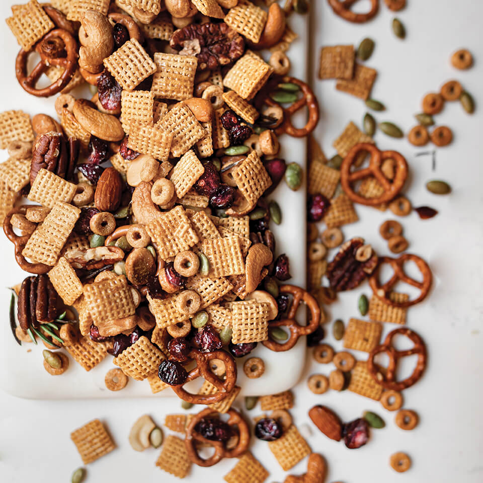 A recipe for Sweet and Salty Chex mix scattered on and spilling over a white marble board