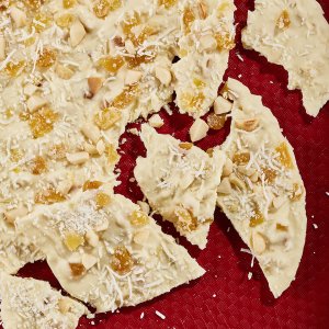 White chocolate bark on a red surface broken into pieces.