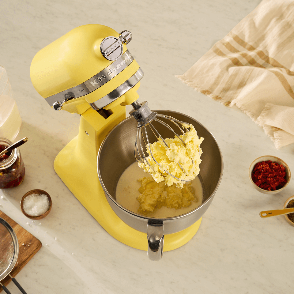 Yellow kitchenaid stand mixer is using a whisk attachment to make butter