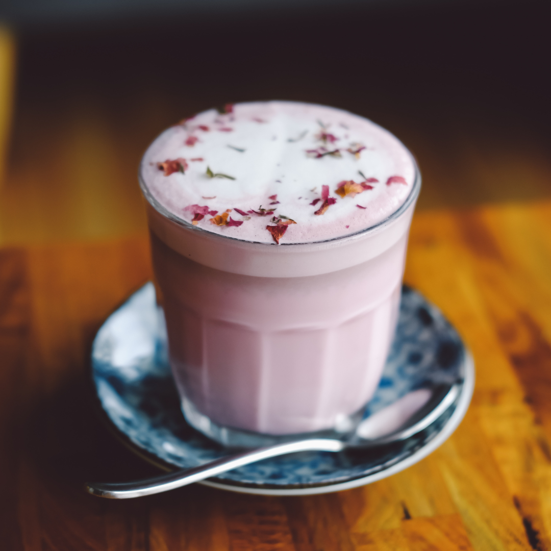 Glass mug of frothy pink coconut rose latte with dried rose petals