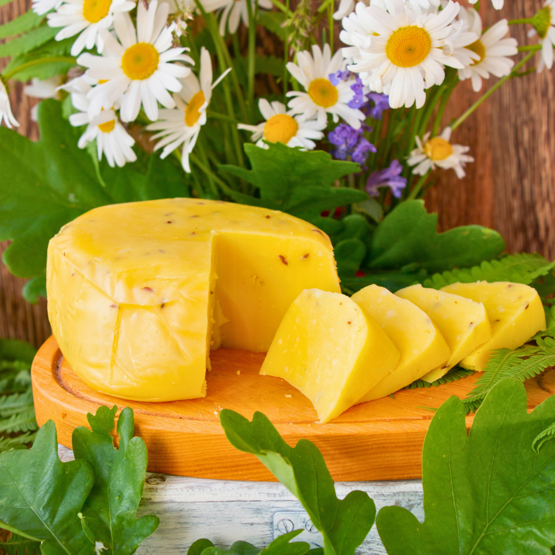 Latvian GI 'Janu siers’ John's Cheese is sitting on a cutting board surrounded by fresh-cut flowers