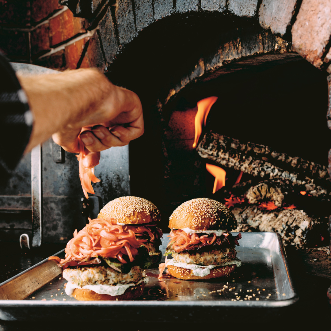 Salmon burgers on a metal tray in front of a wood burning fire